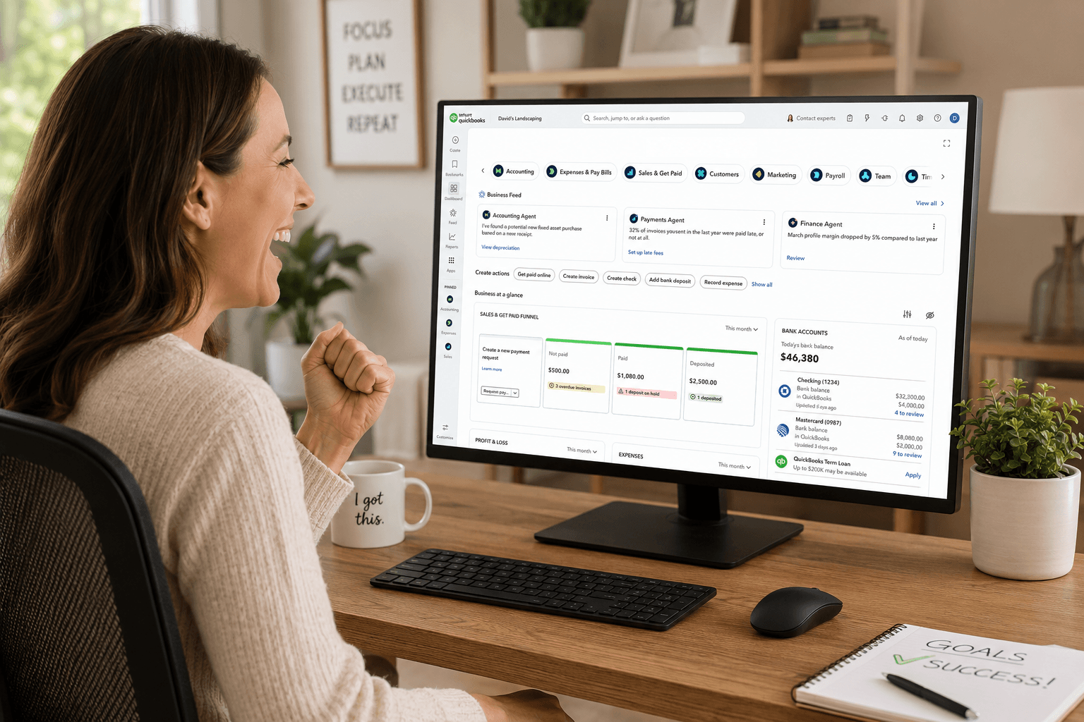 A learner celebrating success at her desk with the QuickBooks Online dashboard on-screen